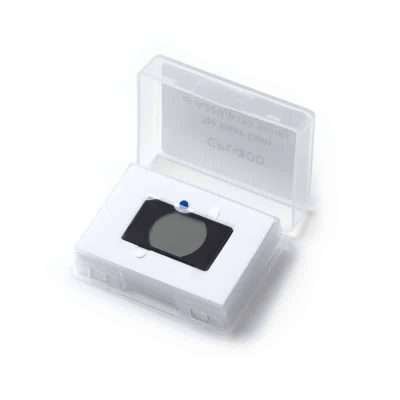 A clear plastic case containing a square glass slide with a small blue dot on it, resting on a white foam pad.